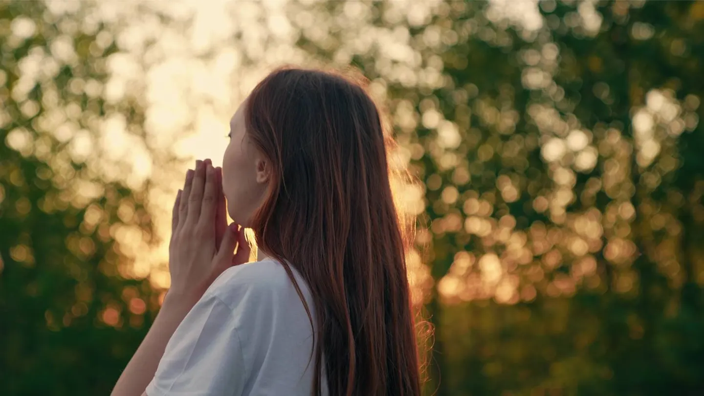 A young woman praying outdoors at sunset