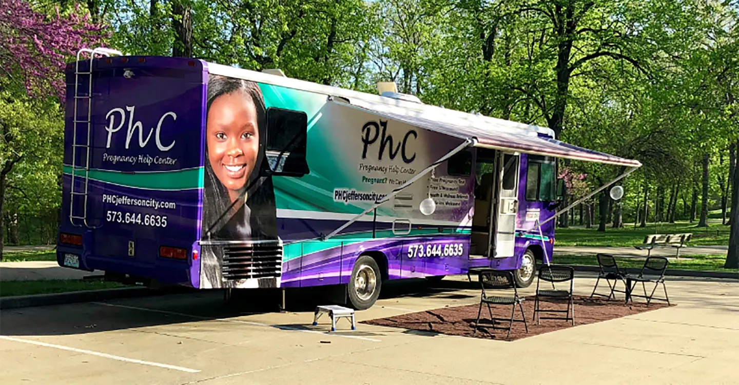 Daisy, the mobile clinic, parked in a park with its awning out and chairs set up